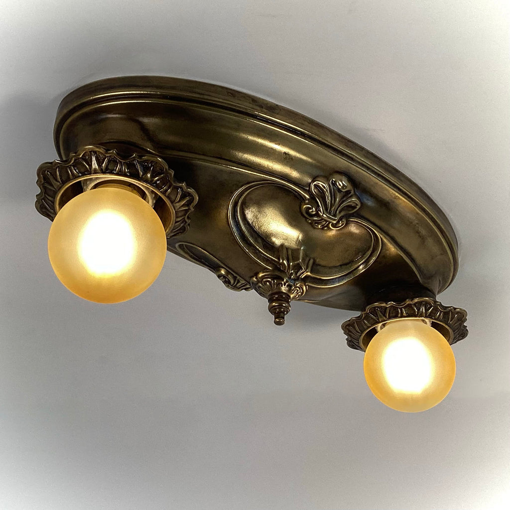 Antique brass two-light flush mount ceiling fixture with illuminated frosted amber bulbs, bottom view.