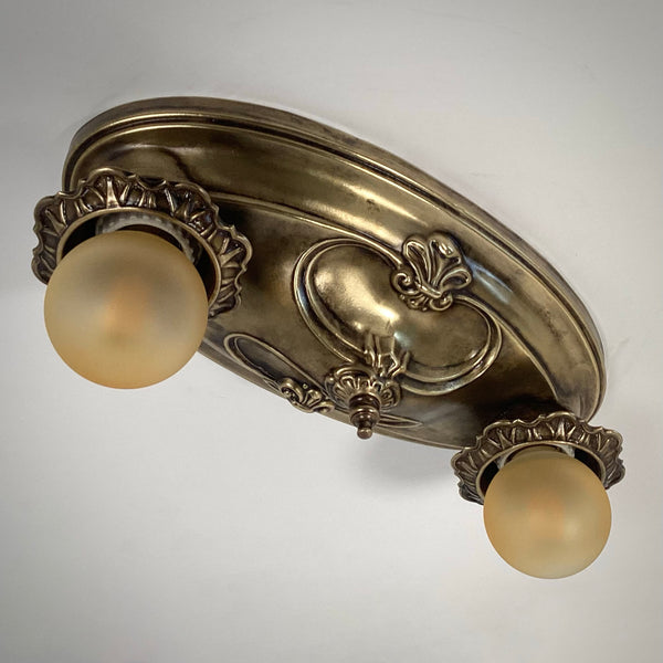 Art Nouveau style two-bulb antique brass flush mount ceiling light turned off, showing textured finish.