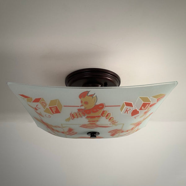 Unlit mid-century nursery flush mount ceiling light with jack-in-the-box and block pattern on bronze fixture.