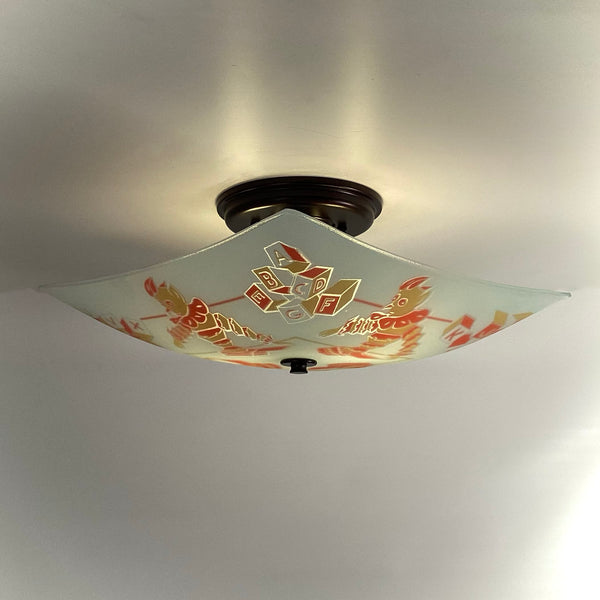 Angled bottom-up view of a lit vintage nursery glass ceiling light showing ABC blocks in center.