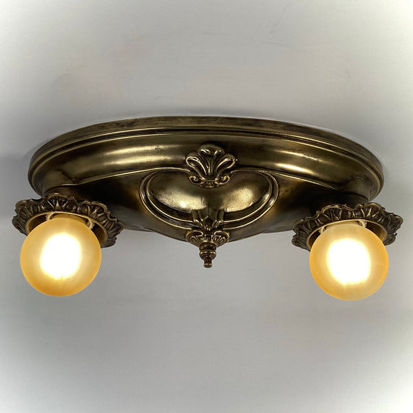Vintage two-socket brass ceiling light fixture with both frosted bulbs turned on, direct angle view.