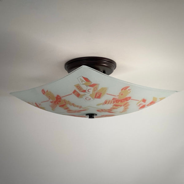 Angled bottom-up view of an unlit nursery glass lamp shade displaying clown graphics and dark bronze mount.