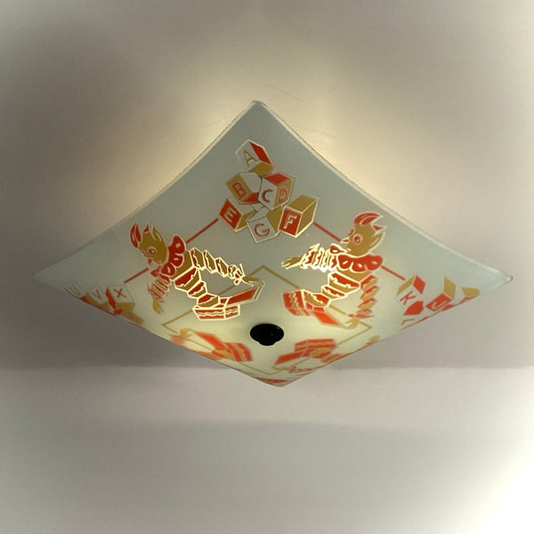Diamond-perspective close-up of a lit retro frosted glass light shade with clown and block illustrations.
