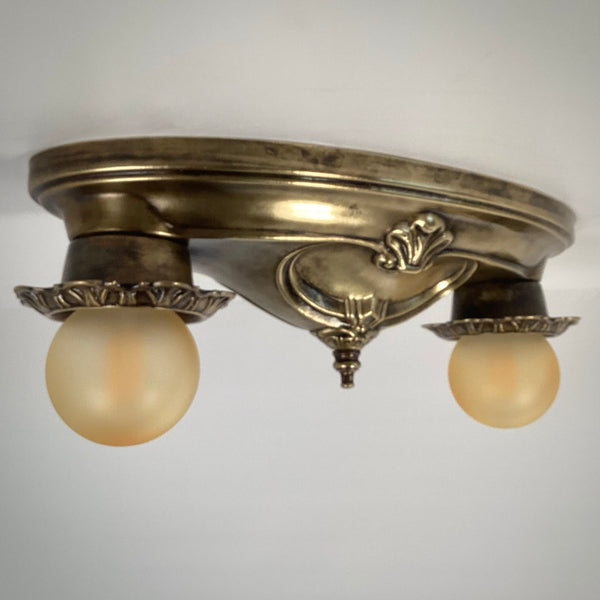 Low-angle profile view of an unlit vintage double-bulb brass ceiling light.