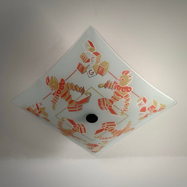 Overhead diamond view of an unlit square nursery lamp shade displaying red and yellow painted graphics.