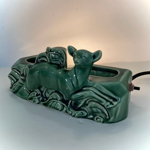 Front angle of a vintage Mid-Century Modern green ceramic doe TV lamp and planter with a soft glow.