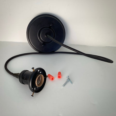 A complete black pendant light kit laid out on a white surface, including the ceiling canopy, cloth-covered cord, bulb socket with shade fitter, orange wire nuts, and mounting screws.