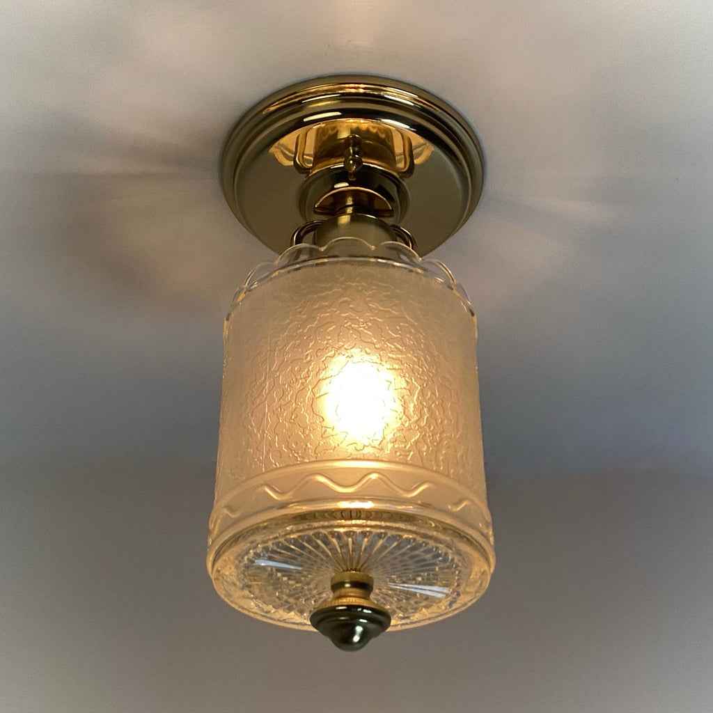 Vintage brass flush mount ceiling light fixture with a textured clear glass shade, illuminated and ceiling-mounted.