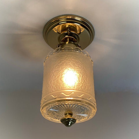 Vintage brass flush mount ceiling light fixture with a textured clear glass shade, illuminated and ceiling-mounted.