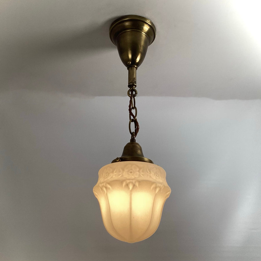 Vintage brass pendant light fixture with illuminated frosted floral glass shade hanging from ceiling chain.