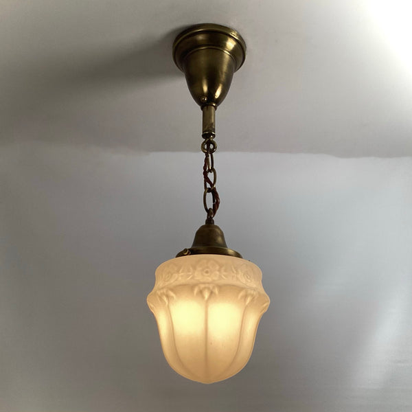 Vintage brass pendant light fixture with illuminated frosted floral glass shade hanging from ceiling chain.