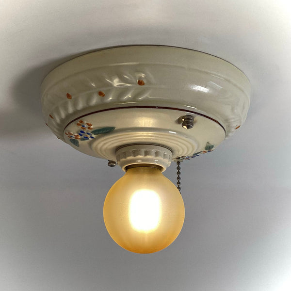 A vintage 1930s Porcelier style ceramic flush mount ceiling light fixture turned on and glowing with a warm amber light against a white ceiling.