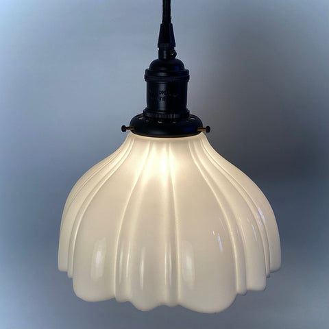 Close-up of a glowing scalloped milk glass pendant light with black hardware.