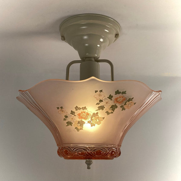 Vintage pink frosted depression glass flush mount ceiling light fixture illuminated with floral pattern.