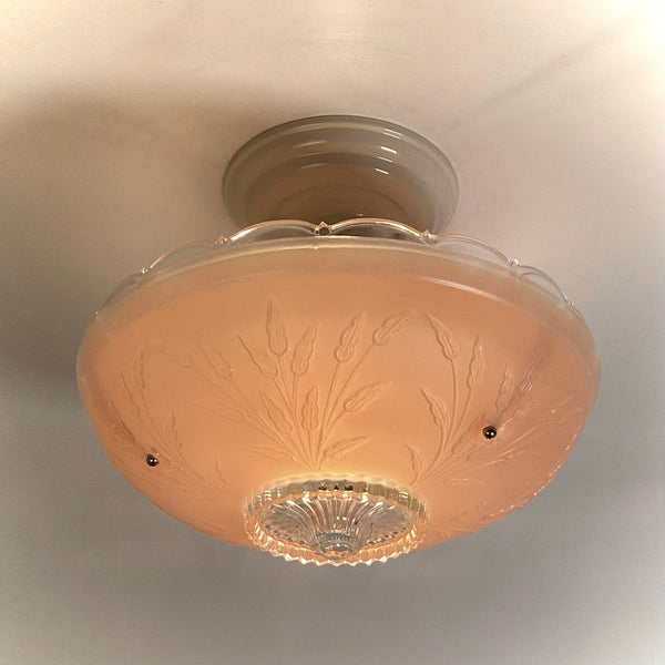 Vintage pink frosted depression glass ceiling light fixture with embossed floral leaf design illuminated on a ceiling.