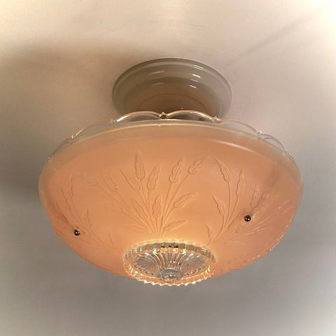 Vintage pink frosted depression glass ceiling light fixture with embossed floral leaf design illuminated on a ceiling.