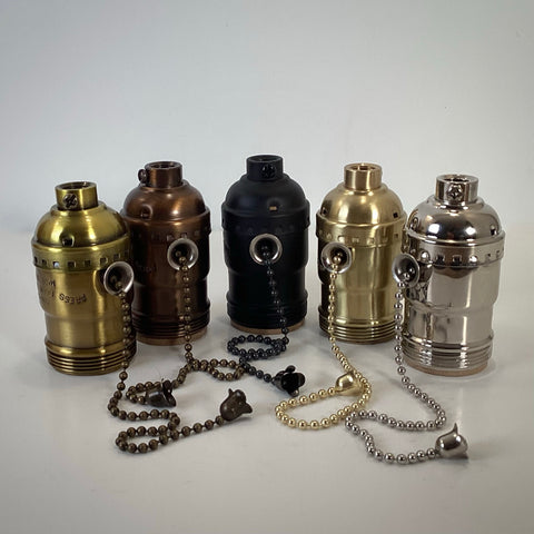 Set of five solid brass UNO pull-chain lamp sockets in assorted finishes including polished brass, antique brass, bronze, satin black, and polished nickel, arranged upright with matching beaded chains.