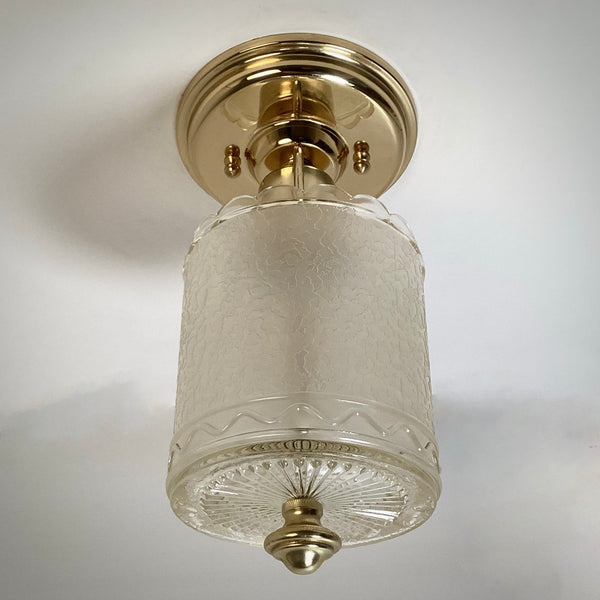 Low-angle unlit shot focusing on the polished brass canopy hardware and cut-glass bottom of a flush mount light.