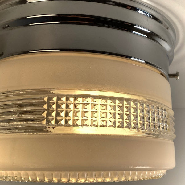 A detailed macro view focusing on the shiny chrome base and the intricate waffle-textured clear glass band of a vintage ceiling fixture.