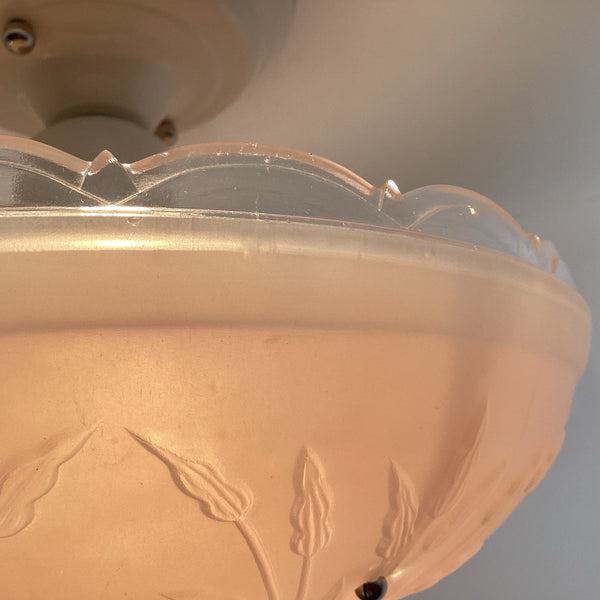 Macro close-up of the scalloped clear glass top edge and embossed leaf details on a pink depression glass shade.