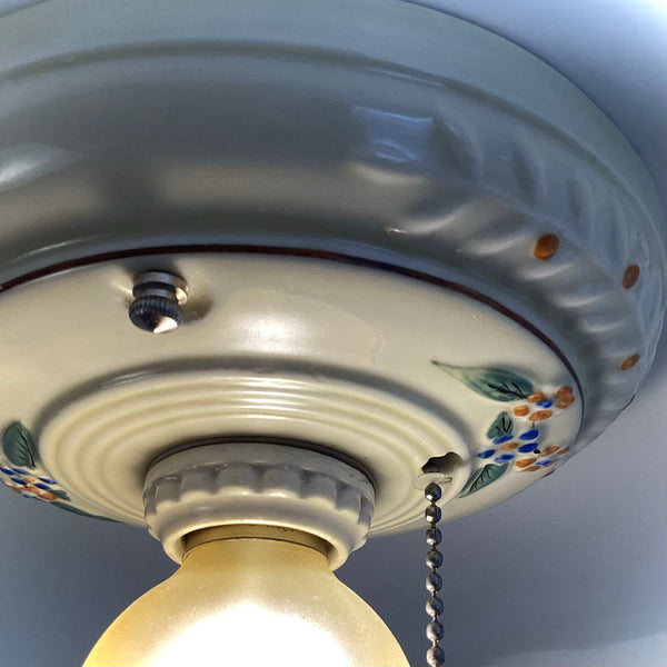 A vintage ceramic ceiling light fixture with a frosted round bulb glowing brightly from a direct bottom angle.