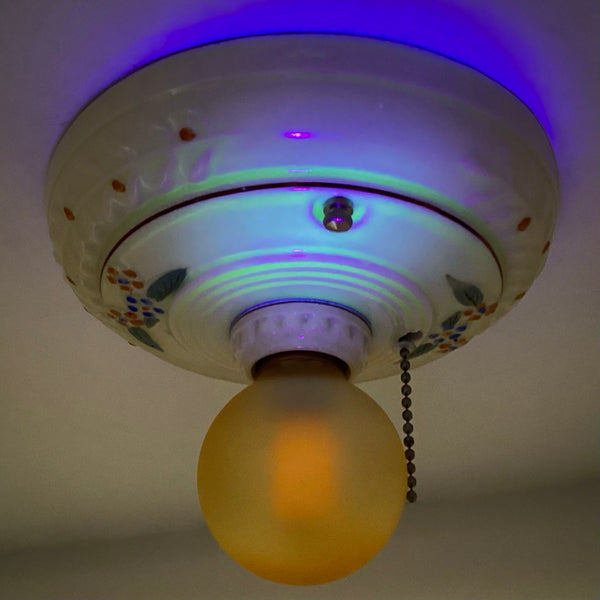 A vintage ceramic ceiling light fixture glowing bright neon green under a UV blacklight, indicating a uranium glaze.
