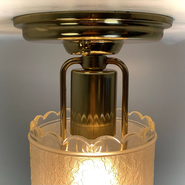 Close-up view of polished brass canopy hardware and socket housing above a scalloped glass light shade.