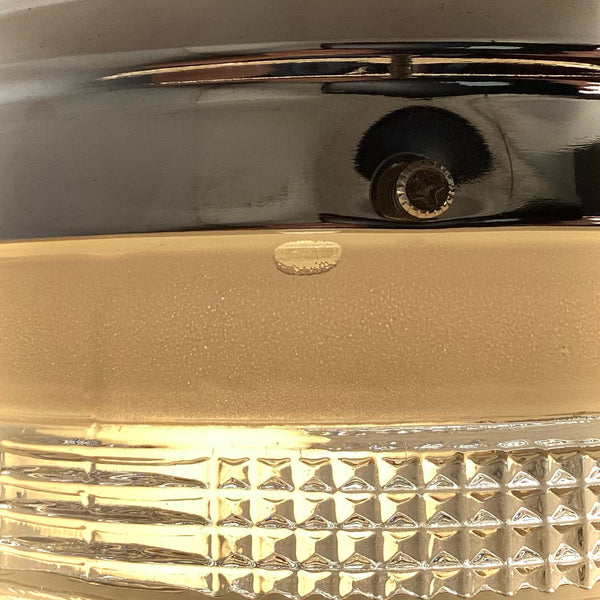 An extreme macro close-up showing a cosmetic imperfection on the rim of a vintage frosted glass ceiling light shade, right below the polished chrome fixture base.