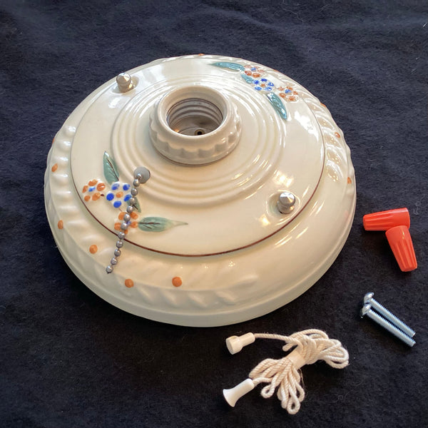 An uninstalled antique porcelain flush mount light fixture body displayed on a black background next to its mounting screws and pull cord.