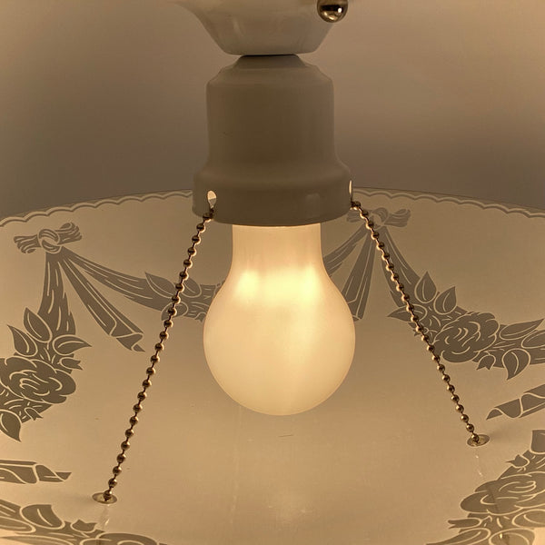 Close up of porcelain socket, pull chain, and bulb on vintage 1950s semi flush ceiling light with frosted floral glass bowl shade