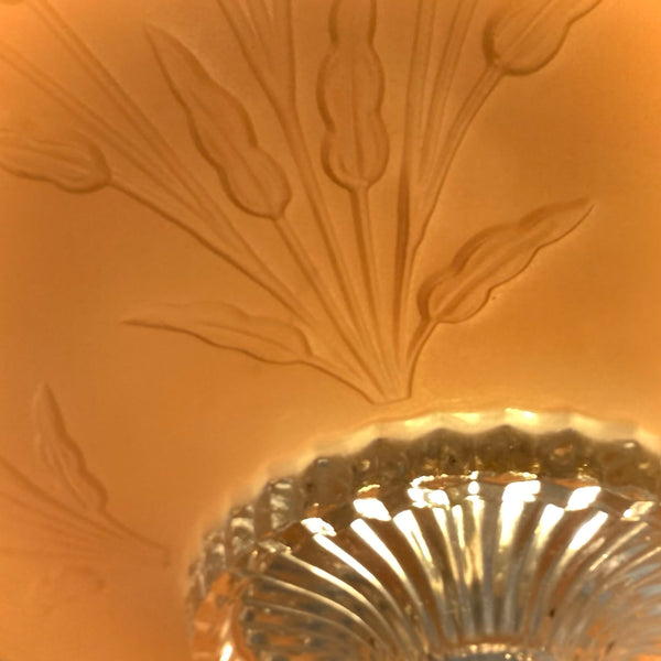 Extreme macro shot showing the clear ribbed glass bottom finial and raised leafy relief pattern on a pink light shade.