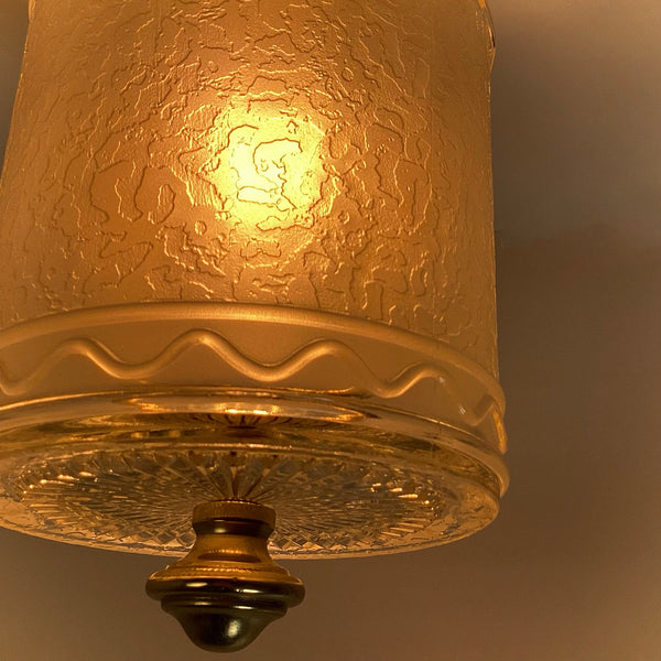 Close-up side view of an illuminated textured glass cylinder shade showing wave motif and brass bottom finial.