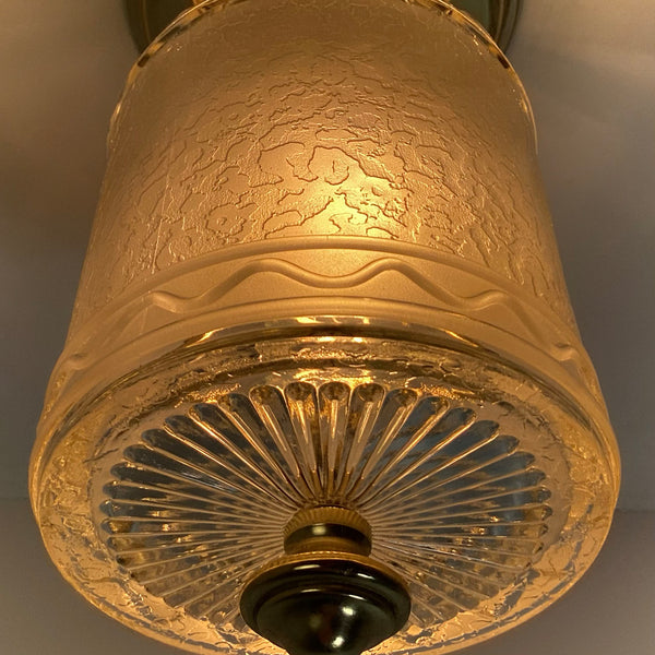 Low-angle close-up of a lit glass ceiling fixture highlighting the sunburst cut-glass bottom and decorative brass knob.