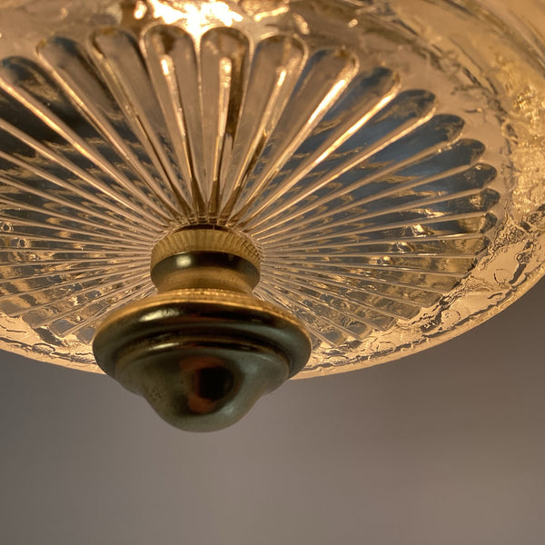 Extreme macro view of a brass bottom finial set against a radial pattern cut-glass ceiling light shade.