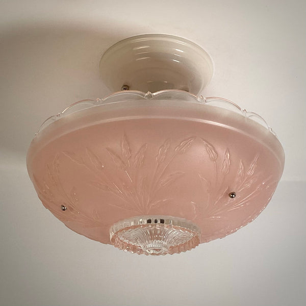 Angled view of a pink frosted glass ceiling shade featuring embossed floral details and clear scalloped rim.