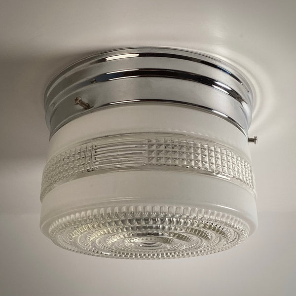 An angled profile shot of a classic retro glass drum ceiling light fixture, turned off, showcasing the frosted and clear waffle-textured pattern.