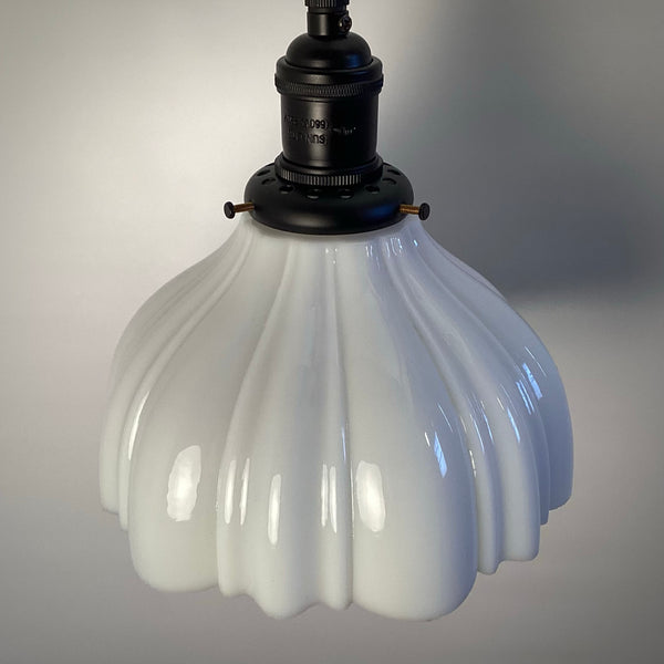 Side view of a white scalloped glass pendant lamp shade off-light.