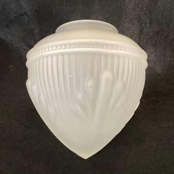 Front view of a vintage frosted white glass light shade showing vertical fluted ridges and decorative molded shell motifs against a dark surface.
