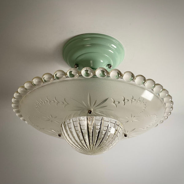 Art Deco style ceiling light fixture with a jadeite green canopy and patterned frosted glass shade turned off.