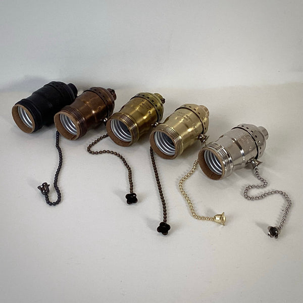 Five brass UNO pull-chain lamp sockets lying on their sides to display the threaded UNO tops and E26 interiors.