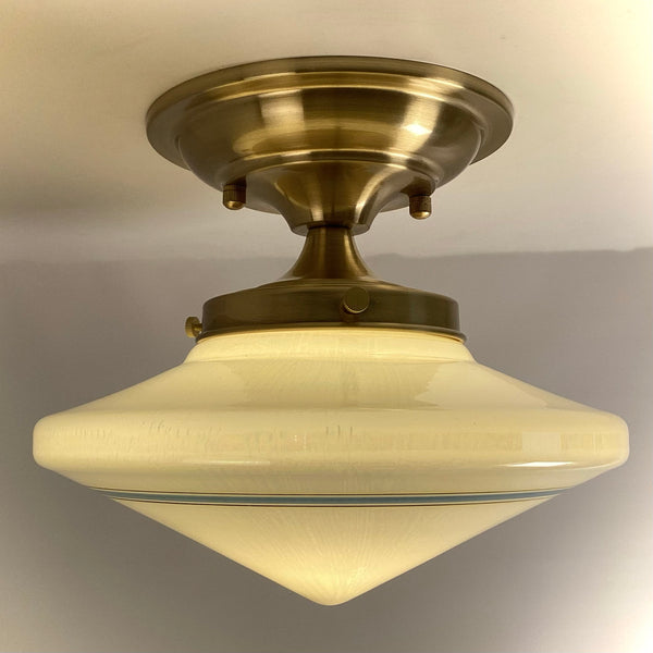 Profile view of an antique milk glass schoolhouse shade with streamlined contours and a subtle blue band, fitted to new satin brass hardware