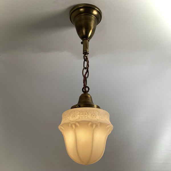 Art Deco style brass chain pendant light fixture turned on, casting warm glow through etched glass shade.
