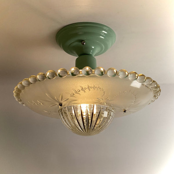 Mid-century semi-flush ceiling light with a green porcelain base and a glowing frosted glass shade.