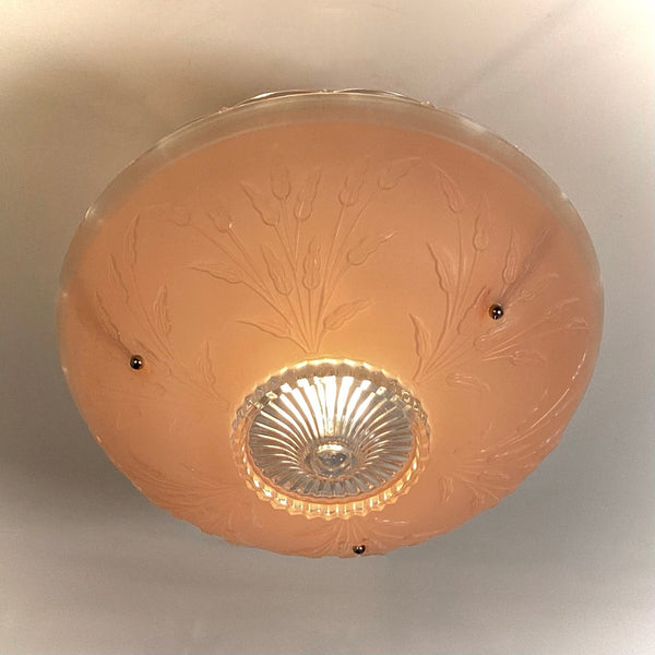 Bottom-up direct view of a round pink glass ceiling shade showing central ribbed clear glass finial center and floral relief pattern.