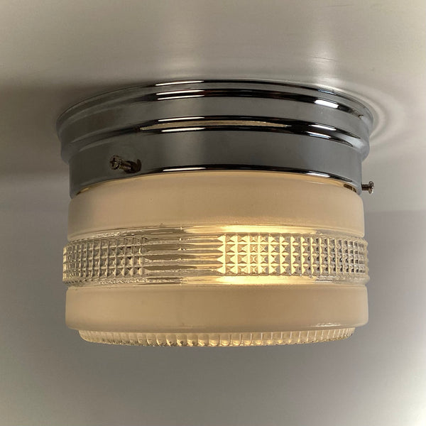 Side profile view of a glowing mid-century modern chrome ceiling light with an intricate geometric pattern on the glass shade.
