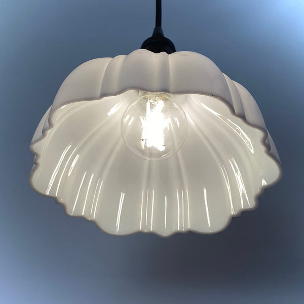 Interior view of a scalloped milk glass pendant light with a lit bulb.