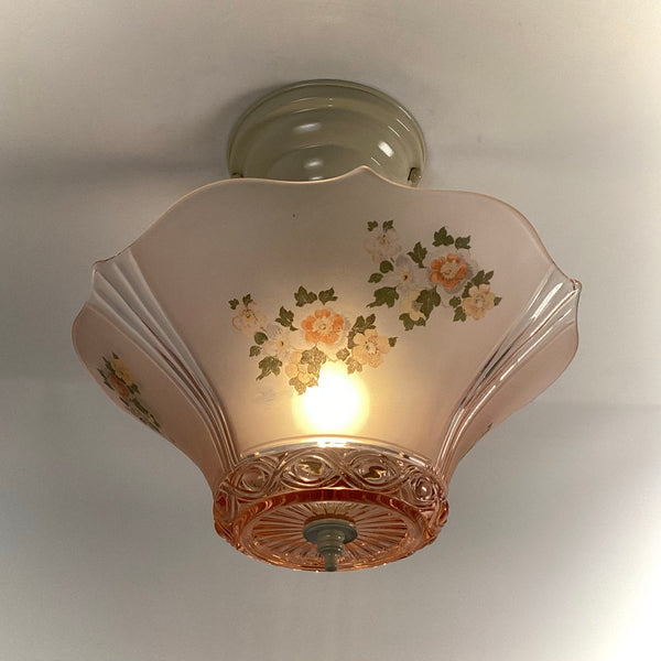 Low-angle view of a pink frosted glass ceiling lamp shade with floral decal and turned-on bulb glowing inside.