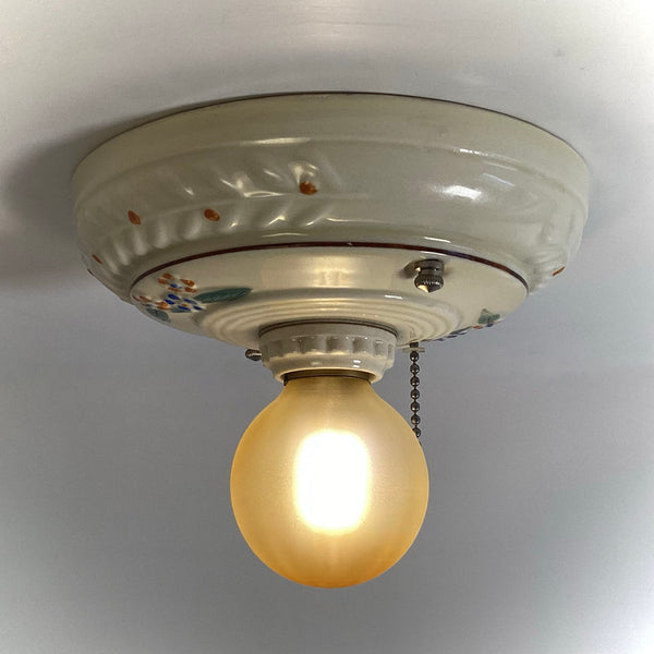 A retro floral hand-painted ceramic ceiling lamp fixture illuminated brightly with a vintage frosted globe bulb.