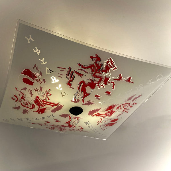 Close-up of a square vintage glass light cover showing a detailed red illustration of a cowboy riding a galloping horse.