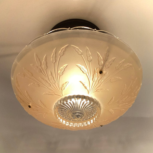 Bottom-up view of an active vintage frosted glass ceiling light highlighting the clear starburst center motif and leaf details.